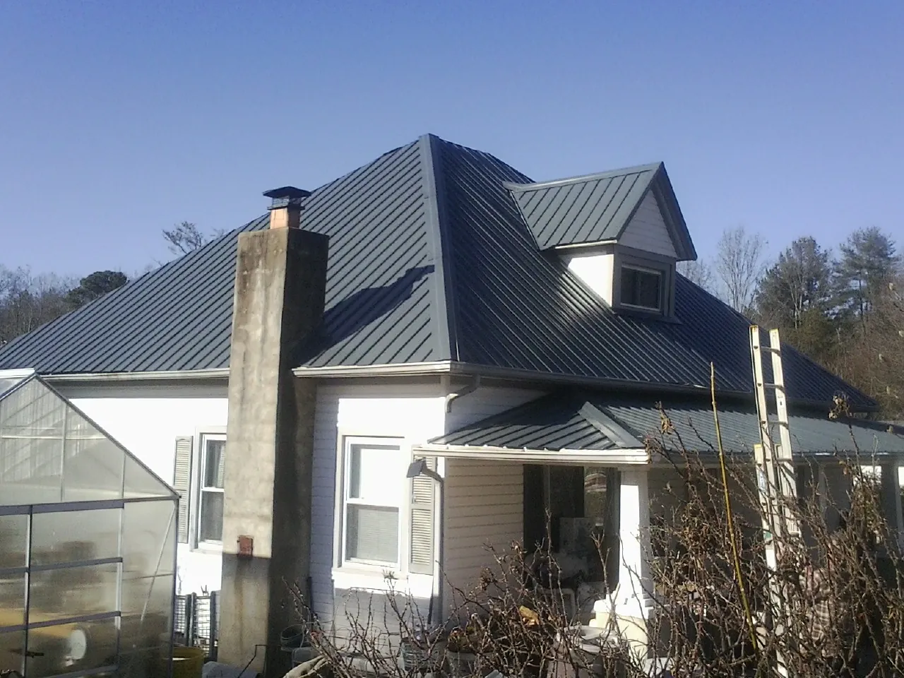 Dark blue standing seam metal roof on a white farmhouse with dormer in Blanchard