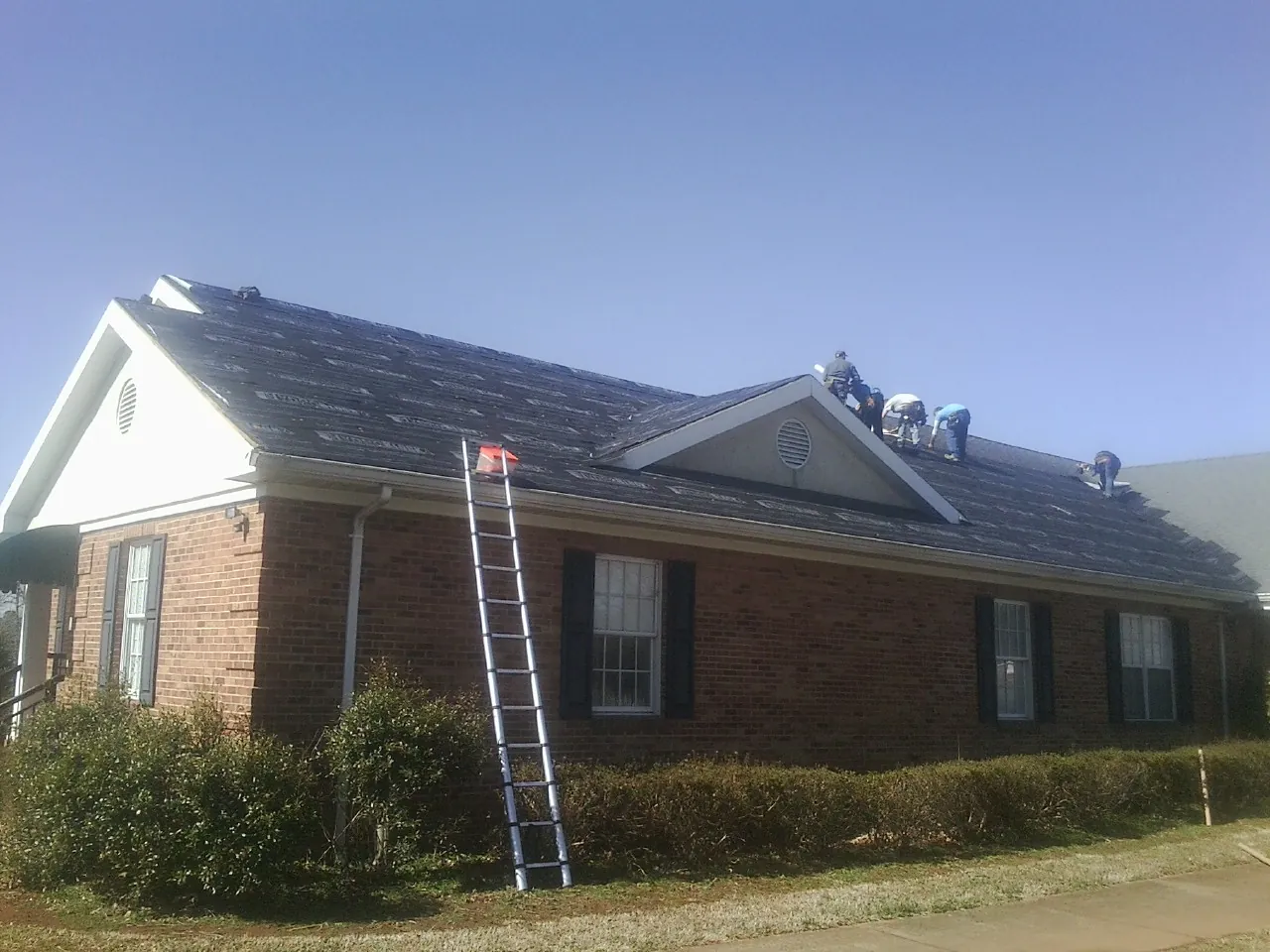Crew tearing shingles off a brick ranch roof with a ladder set — Emergency Roof Repair work by our crew in Blanchard